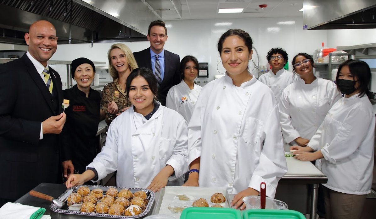 Tina Luu, Siebel Newsom, and group gather in kitchen with frosted scones
